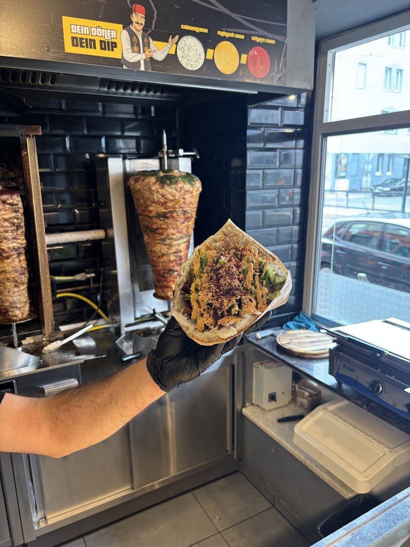 Frisch gefüllter Döner in der Hand vor dem Spieß